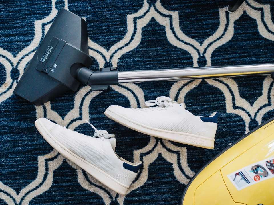 Paar weiße Turnschuhe neben Staubsauger